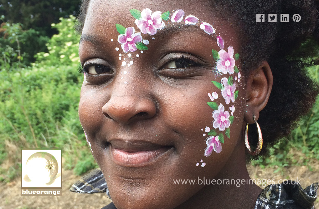 Blue Orange Images face painting, Watford, flower theme with array of pink flowers going from top of nose in a curve to bottom of cheek